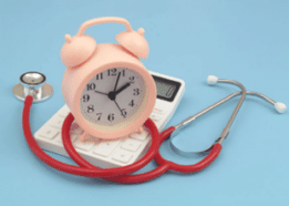 A small pink alarm clock, placed over a white case calculator and a red Stethoscope 